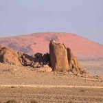 a pile of rocks in a desert with a sand dune in the background